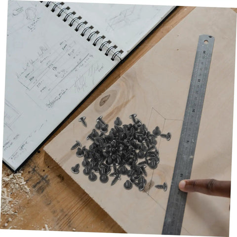 100 Piece Mini Machine Screws For Furniture Repair And DIY Projects Rock Solid Tiny Fasteners scattered on wood with a ruler.