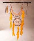 Dream catcher with yellow feathers hanging on a wood stick, featuring circular metal hoop frames and rustic decorations.