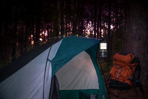 A glowing Siege 540 Lumen Compact LED Camping Lantern With 360 Degree Lighting And Red SOS Mode hanging by a tent at dusk