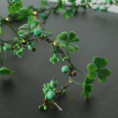 Close-up of faux clover leaf garland with green beads and small LED lights on a dark background.