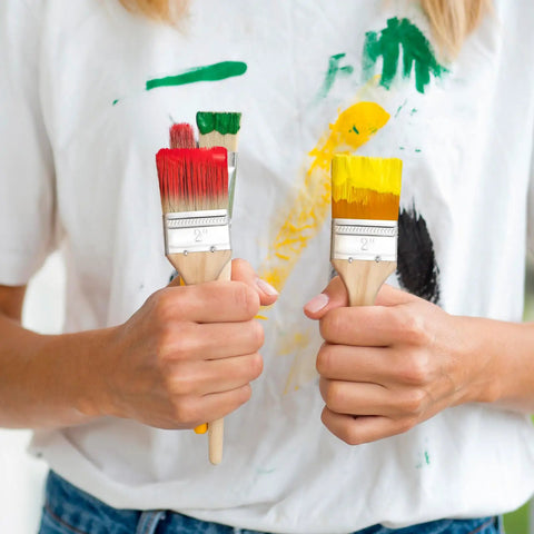 Person holding paint brushes with colored bristles, demonstrating 30 Piece Thick Wood Handle Paint Brush Set With 2 Inch Flat Varnish Brushes For Walls Trim And Deck Stain Heavy Duty Oil Based Paint Tools For Home Improvement And Woodworking.
