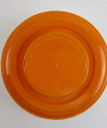 Top view of an orange round container lid, featuring embossed text and a central circular design.