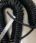 Coiled black power cable with a ruler showing length, part of Built Damn Tough Coiled Extension Cord for job sites.