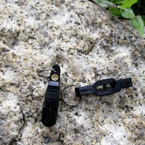 Front view of two black Keproving fishing line clips with O-shaped rings on a rock surface