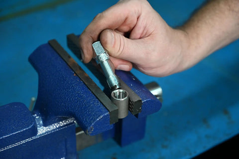Hand using Rethreading Tap 1/4-20NC Thread Repair Tool Set For Damaged Bolt Threads in blue metal vice, showing precision restoration