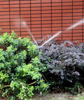 20 Pack Adjustable Farm Sprinkler Irrigation System with counterweight arm watering plants against a brick wall, Black.