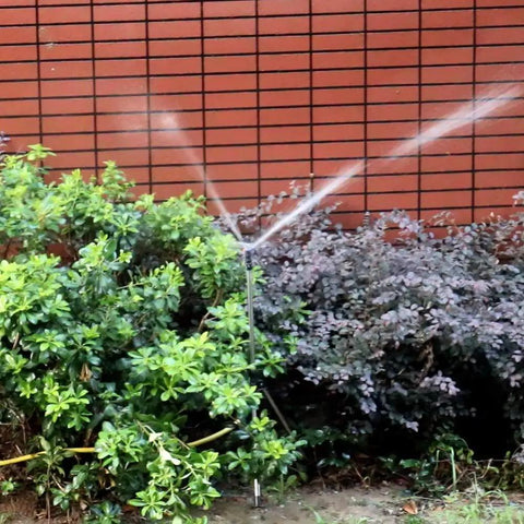 20 Pack Adjustable Farm Sprinkler Irrigation System with counterweight arm watering plants against a brick wall, Black.
