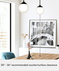 Hepburn 1-Light Modern Brass Pendant Light With Globe Shaped White Glass Shade illuminating a dining room with art and plants.