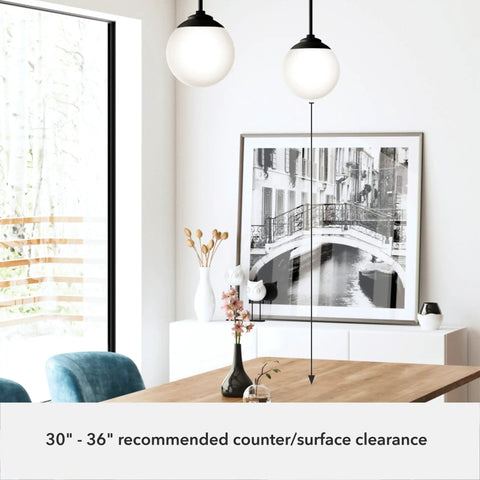 Hepburn 1-Light Modern Brass Pendant Light With Globe Shaped White Glass Shade illuminating a dining room with art and plants.