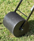 Close-up of Hands On Roller Seeder For Easy Planting No Bend Planting Semi Automatic Metal Garden Seeder on grass