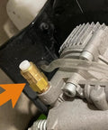 Brass thermal relief valve with white plastic cap on a pressure washer pump, attached clear hose.