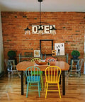 Dining area with Three Light Pendant In Oil Rubbed Bronze With Clear Glass Shades, vintage industrial vibe, above a wooden table and colorful chairs.