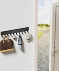 Wall Mounted Key Holder With 10 Hooks No Drill Self Adhesive Matte Black Metal Key Rack for Hallway Home Office Easy Install Keeps Keys Handy In One Spot installed on wall holding bag, keys, umbrella, and hat next to doorway.