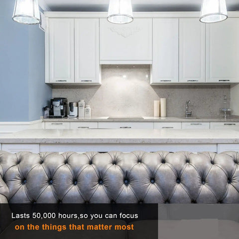 Modern kitchen with white cabinets, grey tufted couch, and counter space illuminated by LED lights lasting 50,000 hours.