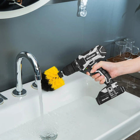 Hand holding Beast Of A 20V Max Cordless Drill Set With Lithium Battery with brush attachment near a running faucet.