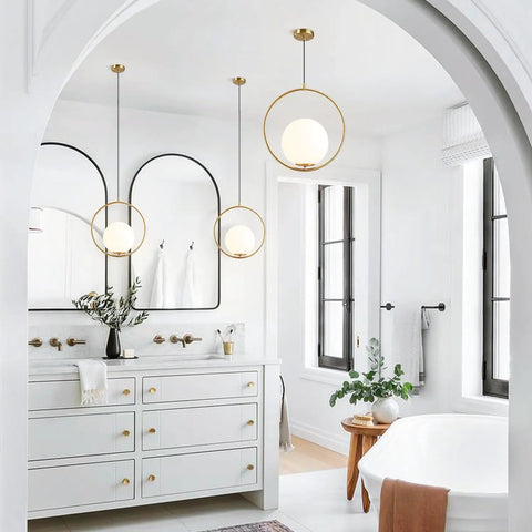 Mid Century Modern Large Globe Pendant Light With Brushed Brass Finish And White Glass Sphere in a bright bathroom.