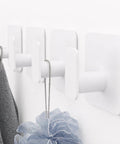 Heavy Duty Adhesive Wall Hooks That Hold Like A Champ, Zero Hassle No Sweat Mounting For Showers And Kitchens, Waterproof Rustproof Sticky Wall Hangers With A Grippy Fit, Kickin Performance Set Of Six White holding a gray cloth and blue loofah.