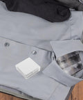 Eighty Piece Pack Of Invisible Adhesive Shirt Collar Stays in a gray shirt inside a suitcase with black socks.