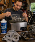 Heavy Duty Ultrasonic Carburetor And Engine Parts Cleaner Concentrate 32 Oz Bottle, mechanic cleaning parts in workshop.