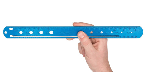 Hand holding blue Spoke Bearing And Cotter Gauge For Bicycles, Handy Wheel Maintenance Tool with easy-read scale and measurements.