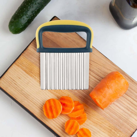 Stainless steel crinkle cutter with blue-yellow ergonomic handle on cutting board, carrot slices nearby.
