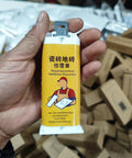 Hand holding Fast Dry Tile Repair Glue Kit For Marble And Granite That Delivers Seamless Crack Chip Hole Fix And Stone Restoration Diy Friendly Durable Non Toxic Formula Clear Cure Two Pack against a background of boxes.