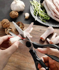 Close-up of hands using scissors to cut chicken feet on a wooden board, with garlic, walnuts, and vegetables nearby