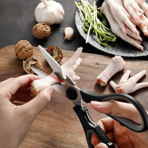 Close-up of hands using scissors to cut chicken feet on a wooden board, with garlic, walnuts, and vegetables nearby