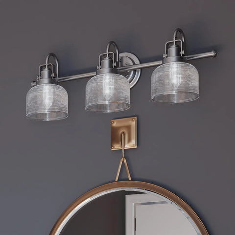 Archie Collection 3-Light Bath Vanity Light With Double Prismatic Glass in Antique Nickel, wall mounted over a round mirror.