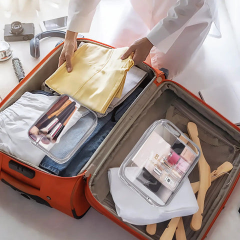 Person packing an open suitcase with a Three Pack Clear PVC Travel Toiletry Bags Set For Women And Men Waterproof See Through Organizer Pouches With Zipper Handles Carry On Airline Friendly Airport Ready TSA Approved Must Have Large Medium Small Bag Kit inside, alongside clothes and travel items.