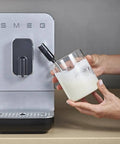 Person frothing milk next to Fully Automatic Coffee Machine With Steam For Home Use Black BCC12BLMUS Six Drink Options