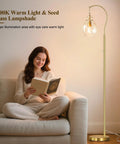 Woman reading next to gold modern floor lamp with globe glass shade, 68 inch tall mid century standing lamp for living room and bedroom.