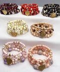 Assorted colorful beaded bracelets with gold heart charms displayed on a white surface in multiple rows.