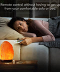 Himalayan Pink Salt Lamp 7 Inches With Upgraded Remote Control and 16 Color Changing Modes on beside table, woman using remote.
