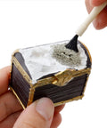 Hand brushing a small treasure chest from the Treasure Chest Dig Kit Party Pack For 12 Kids With 12 Gems And Crystals Excavate Real Treasure
