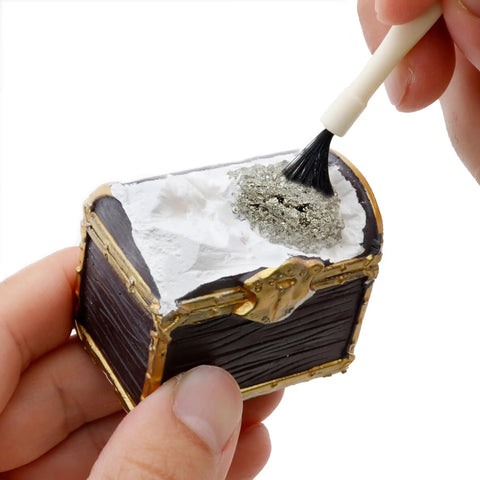 Hand brushing a small treasure chest from the Treasure Chest Dig Kit Party Pack For 12 Kids With 12 Gems And Crystals Excavate Real Treasure