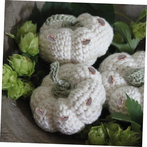 Crocheted white pumpkins with green stems in a decorative arrangement surrounded by green foliage