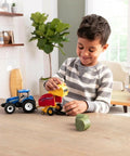 Child playing with New Holland T6 180 1 32 Scale Die Cast Tractor With Roll Belt 560 Round Baler Set and bales on a table.