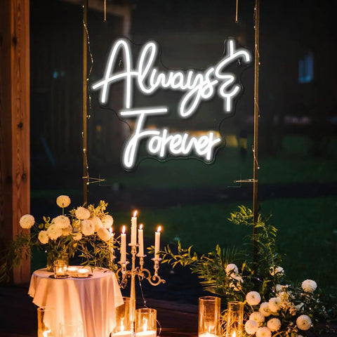 Illuminated 'Always & Forever' white neon sign at an outdoor night event with candles and floral decor in foreground.
