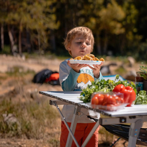 Child holding plate near Foldable Outdoor Picnic Camping Table With Adjustable Height Aluminum Legs And Roll Up Top, Silver Finish