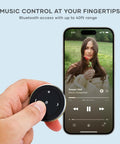 Person holding Bluetooth Media Button With Steering Wheel Mount For Cars And Bikes, Wireless Hands Free Play Pause, Skip Tracks, And Volume Control, Works With iPhone, iPad, Android, MacBook, And All Major Car And Bike Audio Systems, next to smartphone displaying music app.
