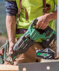 Worker using 36V MultiVolt Brushless Reciprocating Saw Kit with 18V/36V Battery, cutting wood at a construction site, close-up.