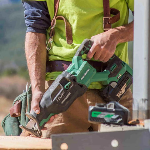 Worker using 36V MultiVolt Brushless Reciprocating Saw Kit with 18V/36V Battery, cutting wood at a construction site, close-up.