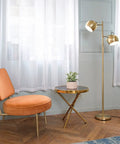 Miles 61 Inch Two Light Floor Lamp in Matte Brass Finish with Adjustable Heads beside a chair and table in a living room.