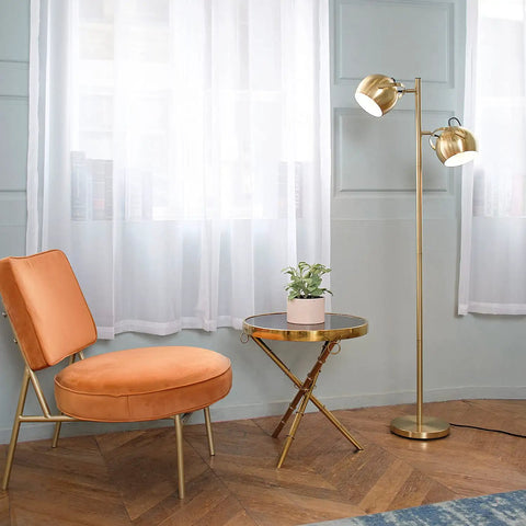 Miles 61 Inch Two Light Floor Lamp in Matte Brass Finish with Adjustable Heads beside a chair and table in a living room.