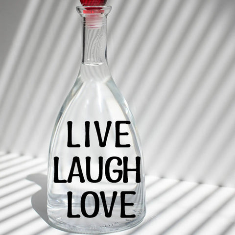 Glass bottle with 'Live Laugh Love' phrase in black vinyl letters, showcasing part of the 1260 Pcs Dope Vinyl Letter Stickers Set In 10 Sheets Black Self Adhesive Numbers Punctuation For Mailbox Signs Windows Doors Cars Trucks Home And Business Address Plaque One Inch Size Weatherproof Durable.