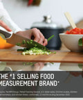 Person chopping green onions with chef's knife beside red bell pepper and measuring cup on a kitchen counter