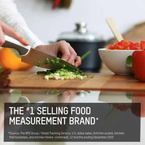 Person chopping green onions with chef's knife beside red bell pepper and measuring cup on a kitchen counter
