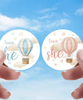 Person holding 40 Count Pink and Blue Hot Air Balloon Gender Reveal Stickers for Team He and Team She, 1.75 Inch Round Labels.