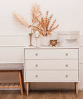 Stylish dresser with three drawers, white finish, decorated with golden accents and dried foliage for a chic look.